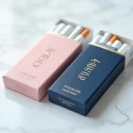 Deux paquets de cigarettes Vogue côte à côte sur marbre blanc, version pastel rose et version bleue marine, comparaison des couleurs d'emballage