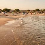 Plage de sable méditerranéenne ensoleillée proche de Nîmes avec parasols colorés et baigneurs au bord de l'eau en été